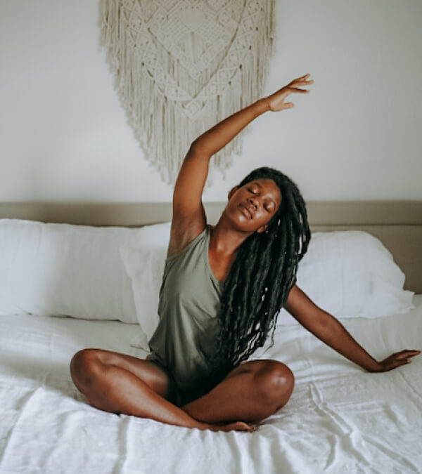 Woman doing a relaxing side stretch in bed, wearing a sage lounge tank