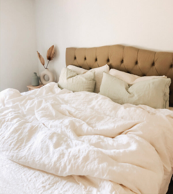 Bed made up in rumpled cream linen sheets.  Everything in the room is beige.