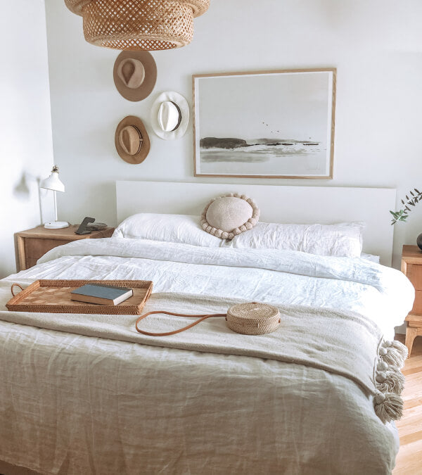 Bed made up in rumpled cream linen sheets.  Everything in the room is beige.  3 hats hanging on the wall