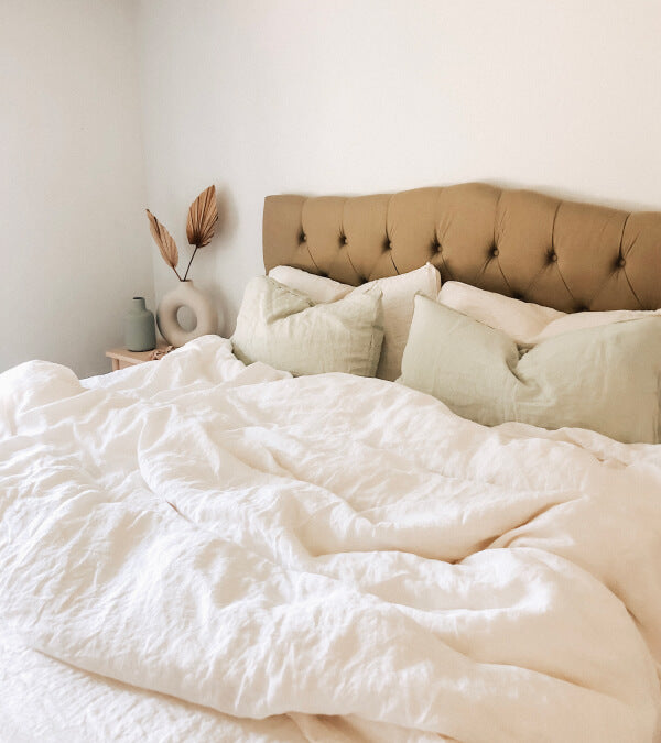 Bed made up in rumpled cream linen sheets.  Everything in the room is beige