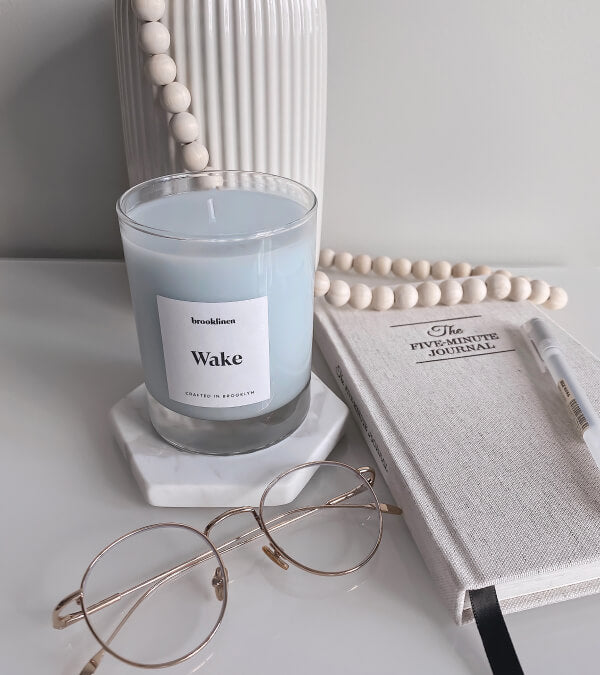 Wake candle next to a pair of glasses and a journal