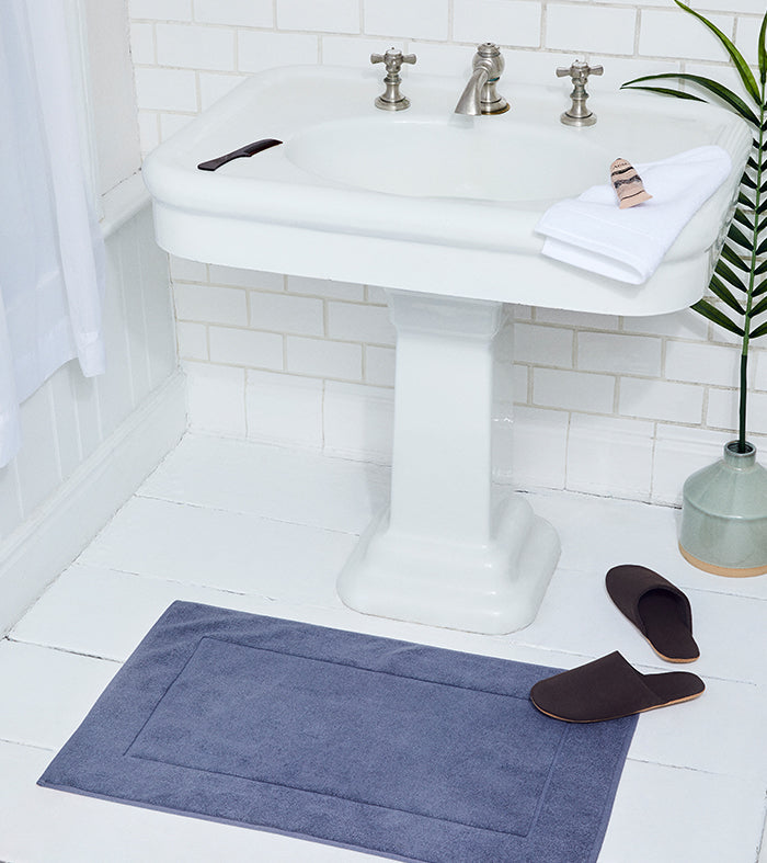 Grey bath mat in front of a white pedestal sink