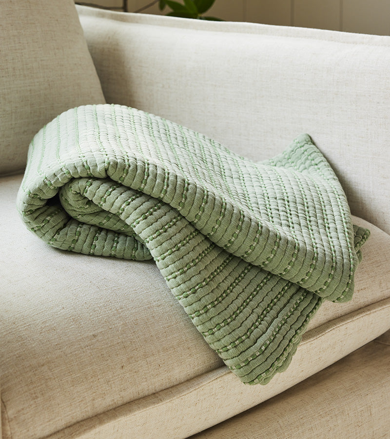 A green Lightweight Textured Throw Blanket flopped onto a firm, earth-toned couch.