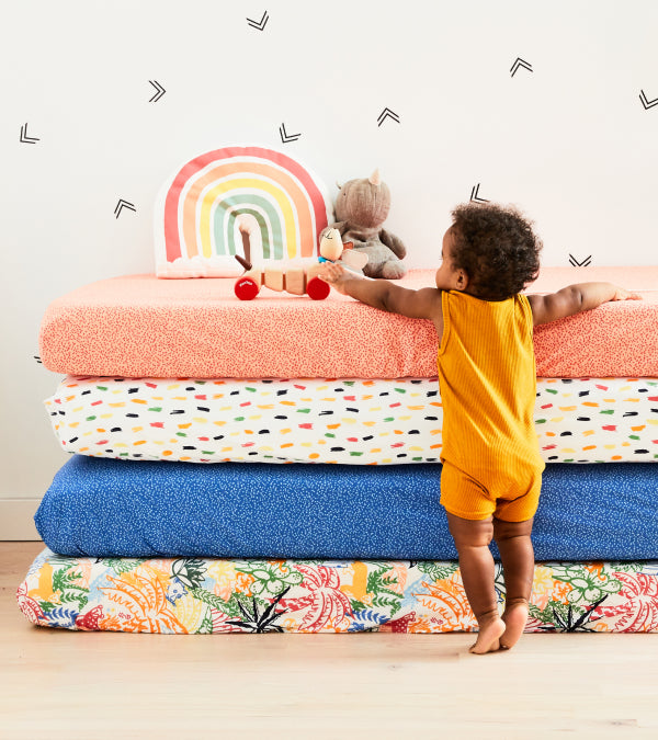 A cute kid playing with a toy that is on top of 4 mattresses with each pattern of sheets
